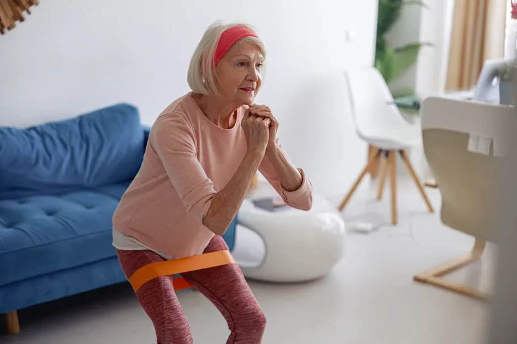 An older woman using a resistance band around her legs for a home squat exercise