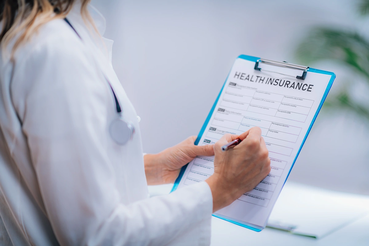 A clinician reviewing a health insurance coverage form on a clipboard
